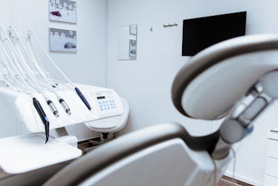 A clean and modern dental examination room with a dental chair, a dental unit with various tools, a wall-mounted monitor, and abstract artwork on the wall.